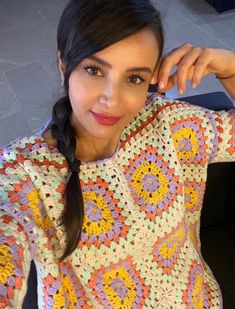 a woman sitting at a table wearing a colorful crochet sweater and holding her hand on her shoulder