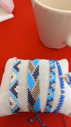 a stack of bracelets sitting on top of a pillow next to a coffee cup