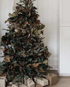 a christmas tree with presents under it in front of a white wall and wooden floor