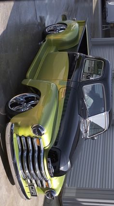 an old green truck parked in front of a garage door with its hood up and windows open