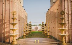 the entrance to an outdoor wedding venue with gold pillars and flowers on it's side