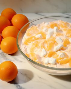 oranges and whipped cream in a glass bowl on a marble counter top next to some oranges