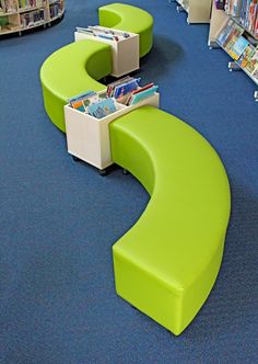 a green curved bench sitting in the middle of a library filled with children's books