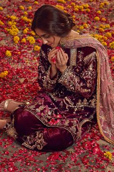 a woman sitting on the ground with flowers all around her and holding something in her hand