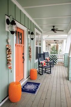 two rocking chairs on the front porch of a house with an orange door and blue rug