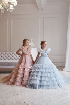 two women in dresses standing next to each other near a couch and chandelier