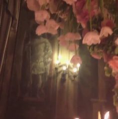 flowers and candles are lit in front of a wall with an image on it at night