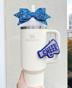 a person holding up a starbucks cup with a blue bow on the top and name charm attached to it