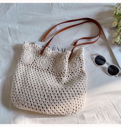 a crocheted bag sitting on top of a bed next to sunglasses and a book