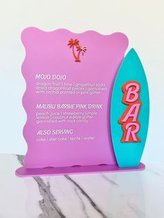 a pink and blue sign sitting on top of a marble counter next to a surfboard