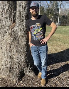 a man standing next to a tree with his hands on his hips