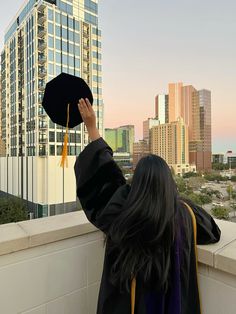 a woman wearing a graduation cap and gown is looking at the city from her balcony