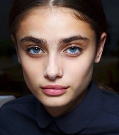 a young woman with blue eyes and dark shirt looks at the camera while sitting down