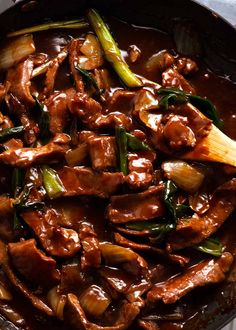 a skillet filled with meat and vegetables on top of a table next to a wooden spoon