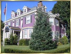 a large purple house with a flag on the front lawn and trees in front of it