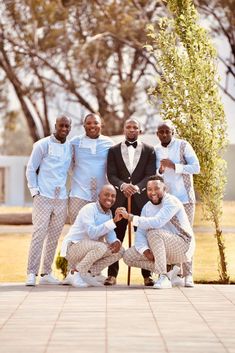 a group of men standing next to each other in front of a tree and building