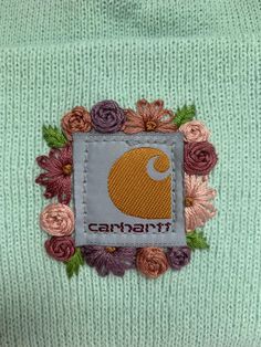 the back of a green sweater with flowers and an embroidered patch on it that says canarit