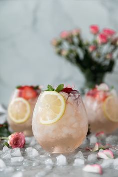 three glasses filled with lemonade and strawberries on top of crushed ice next to flowers