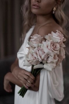 a woman wearing a white dress holding a bouquet of flowers in her hand and looking off to the side