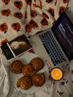 an open laptop computer sitting on top of a bed next to pastries and candles