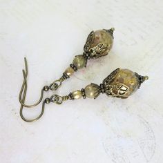 These lovely earrings feature premium Czech glass beads.  The color of the beads is a beautiful cream/ivory with gorgeous picasso accenting.  The beads have an opal effect which gives them a warm golden inner glow with movement and light changes.  They are absolutely STUNNING! I have hand wired and layered them in antiqued brass filigree.  All components are of the utmost quality and lead free and nickel free for your comfort and ease of wear.   Antiqued brass French hook ear wires complete the Unique Gold Czech Glass Jewelry, Handmade Czech Glass Vintage Earrings, Elegant Czech Glass Earrings With French Hook, Elegant Czech Glass Crystal Earrings, Vintage Gold Czech Glass Earrings, Crazy Shirts, Outfit Aesthetics, Victorian Earrings, Inner Glow