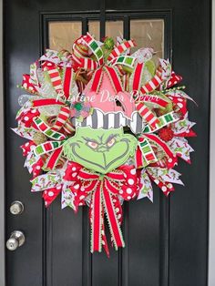 a christmas wreath with the grin face on it is hanging on a black front door