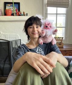 a woman holding a pink stuffed animal in her arms and smiling at the camera while sitting on a couch