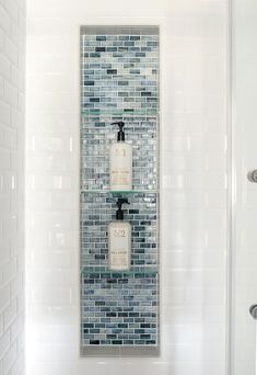 a glass shelf with two bottles on it in a white tiled bathroom, next to a shower door