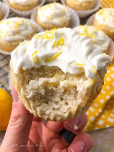 a person holding up a cupcake with frosting and lemons in the background