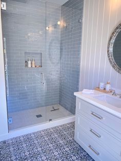 a bathroom with a walk in shower next to a white sink and counter top under a round mirror