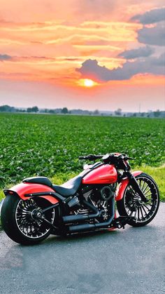 a red and black motorcycle parked on the side of a road near a green field