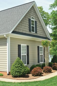 a house that is in the grass with bushes around it and trees on either side