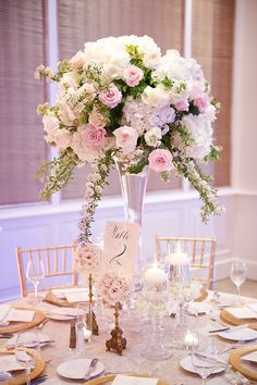 a tall vase filled with white and pink flowers on top of a dining room table