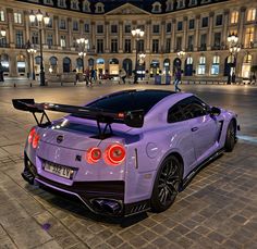 a purple sports car parked in front of a large building at night with its lights on