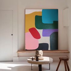 an abstract painting hangs on the wall above a small table with stools in front of it