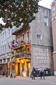 people walking on the sidewalk in front of a building with an advertisement for ginger mint juice