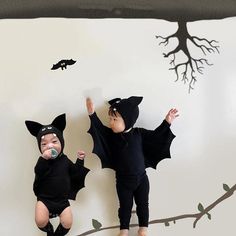 two babies dressed up in halloween costumes on a tree branch with bats flying above them