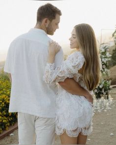 a man and woman standing next to each other in front of flowers on the ground