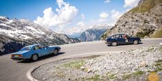 two cars driving down a mountain road with mountains in the background