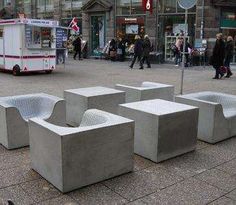 several concrete seats sitting on the ground in front of a building with people walking by