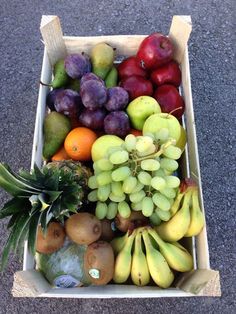 a cardboard box filled with lots of different types of fruit on the ground next to each other