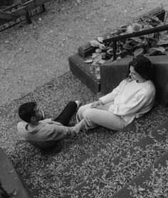 black and white photograph of two people sitting on the ground next to each other talking