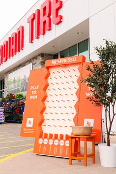 an orange sign sitting in front of a store next to a small potted tree