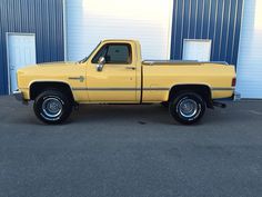 a yellow pick up truck parked in front of a blue warehouse building with two doors