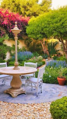 an outdoor table and chairs are in the middle of a garden with trees, shrubs, and flowers