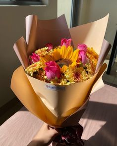 a bouquet of sunflowers and roses wrapped in brown paper on top of a table