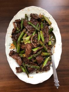 beef and asparagus stir fry on a white plate with a fork next to it