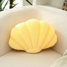 a scallop shell shaped pillow sitting on top of a white couch next to a potted plant