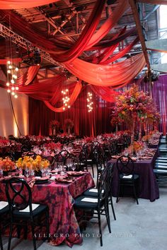 a banquet hall with tables covered in purple and red cloths, chandeliers and floral centerpieces