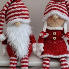 two red and white knitted christmas gnomes sitting on a shelf next to each other